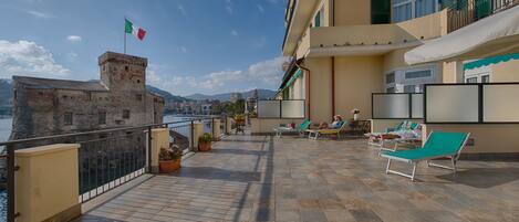 Una terraza con vistas al mar y a las montañas, con sillones de descanso y plantas en macetas.