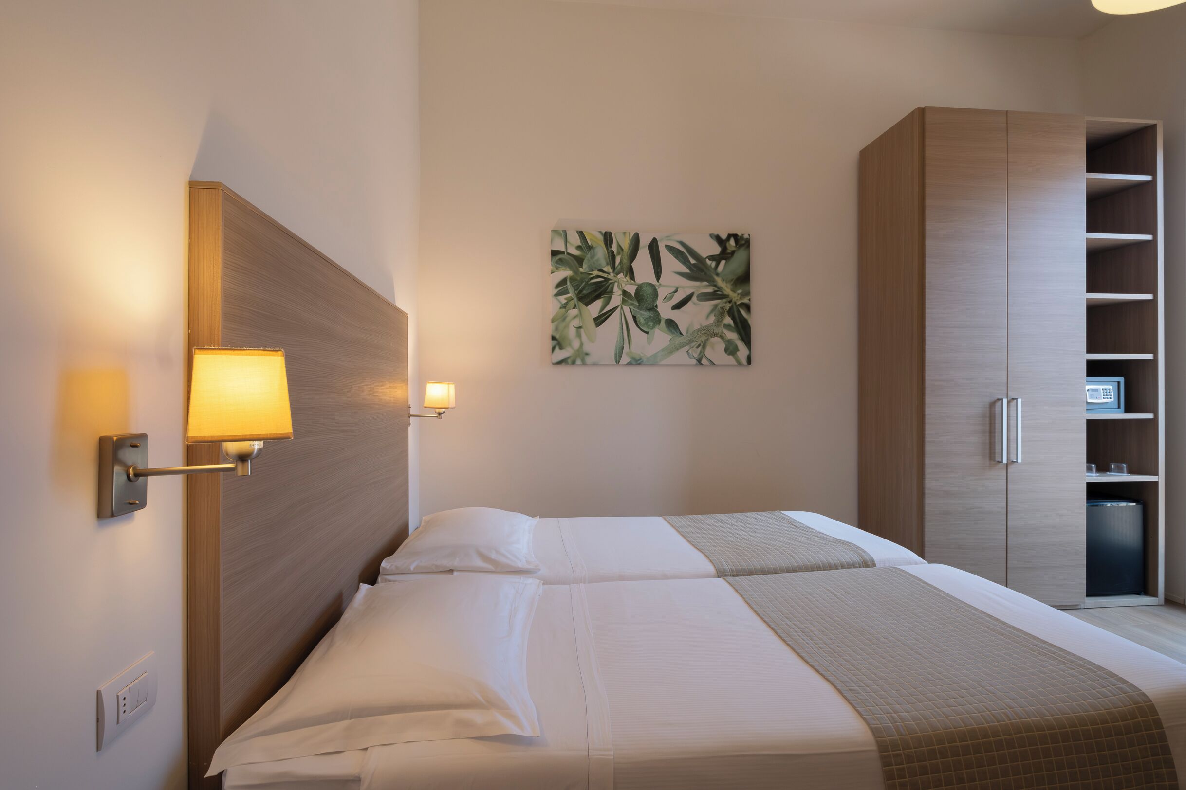 Een hotelkamer met een bed, een wandlamp, een houten garderobe en een kunstwerk aan de muur.