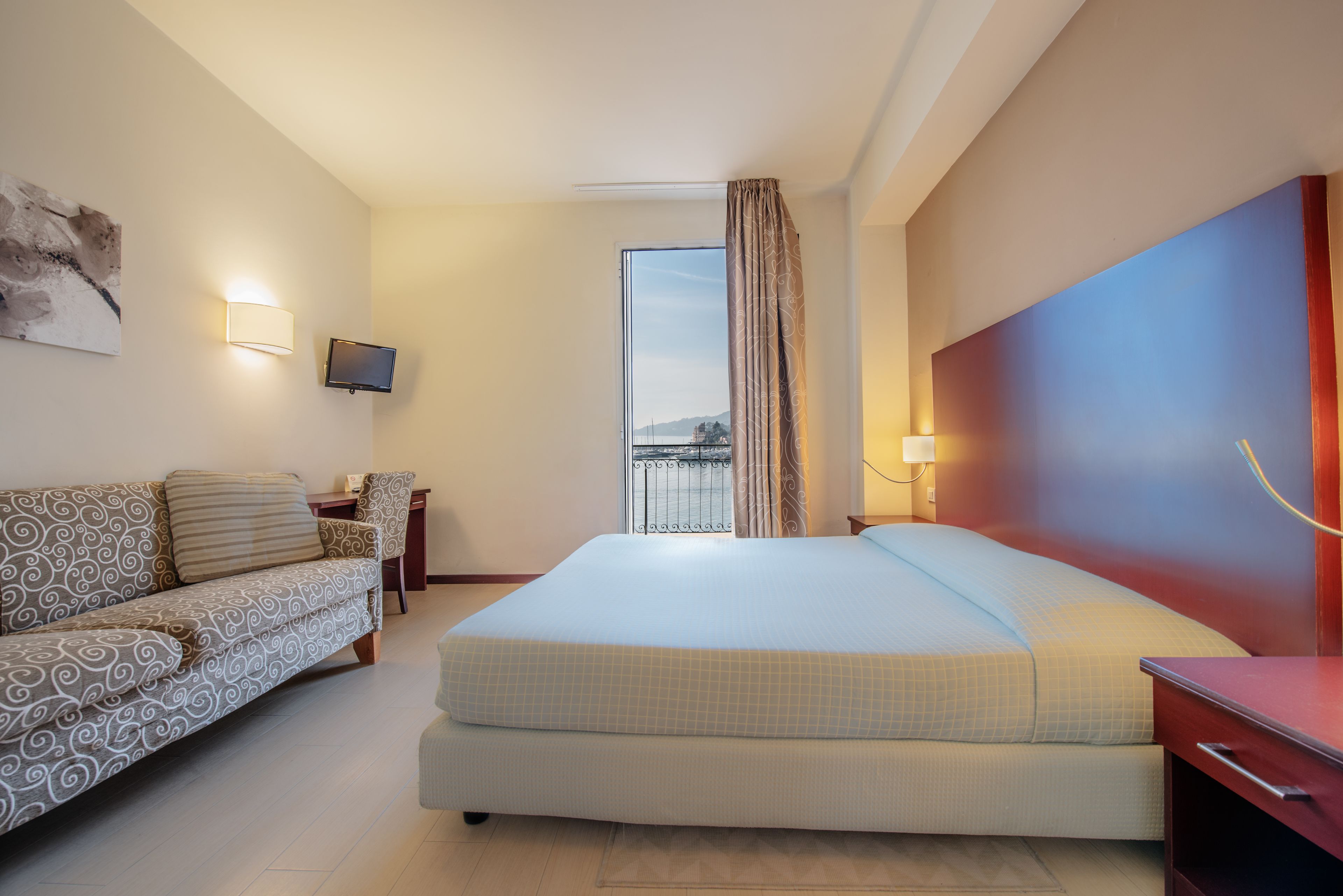 Een hotelkamer met een bed, een bank, een televisie en uitzicht op de omgeving.