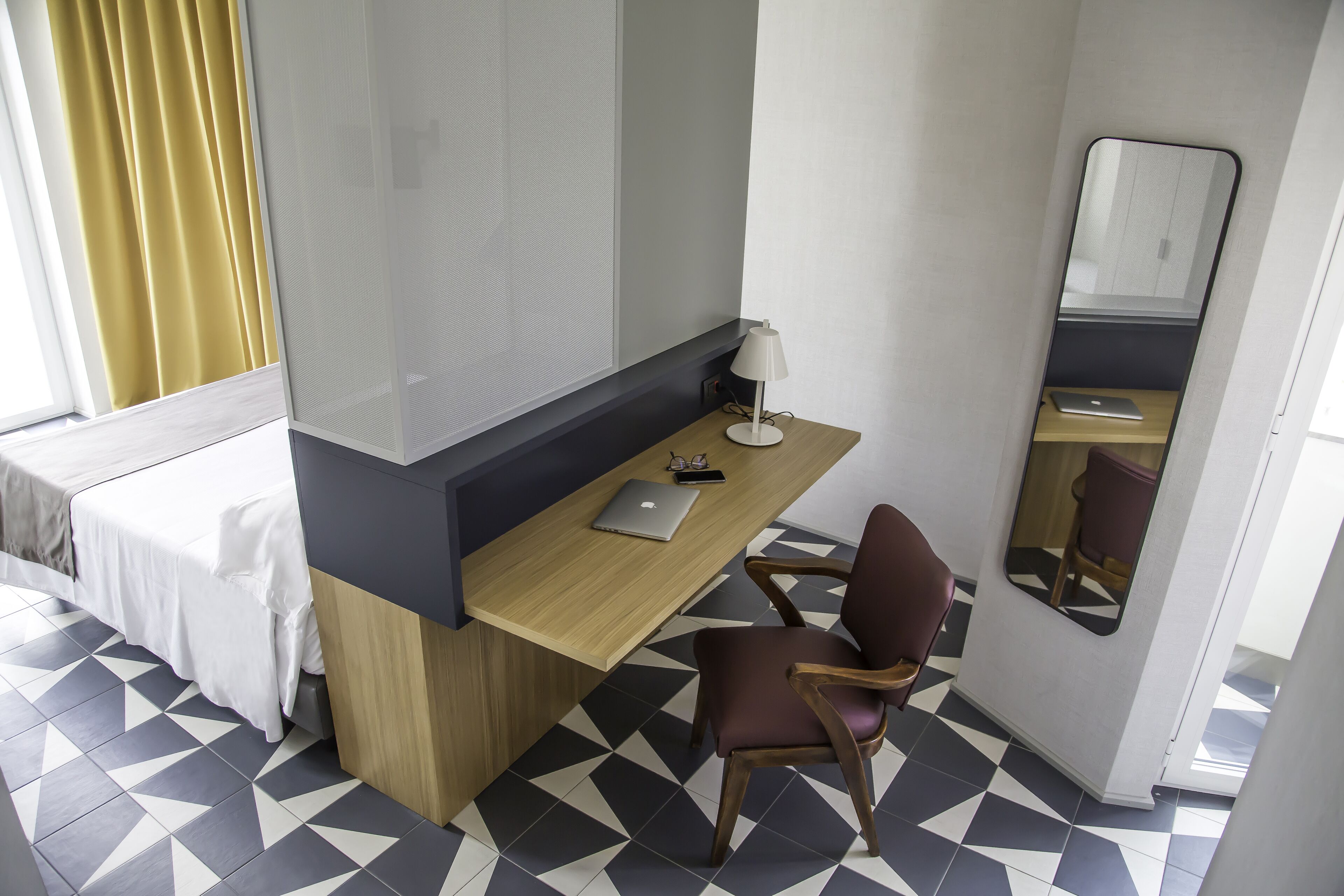 Une chambre d’hôtel avec un lit, un bureau avec un ordinateur portable, une chaise, une lampe et un miroir.