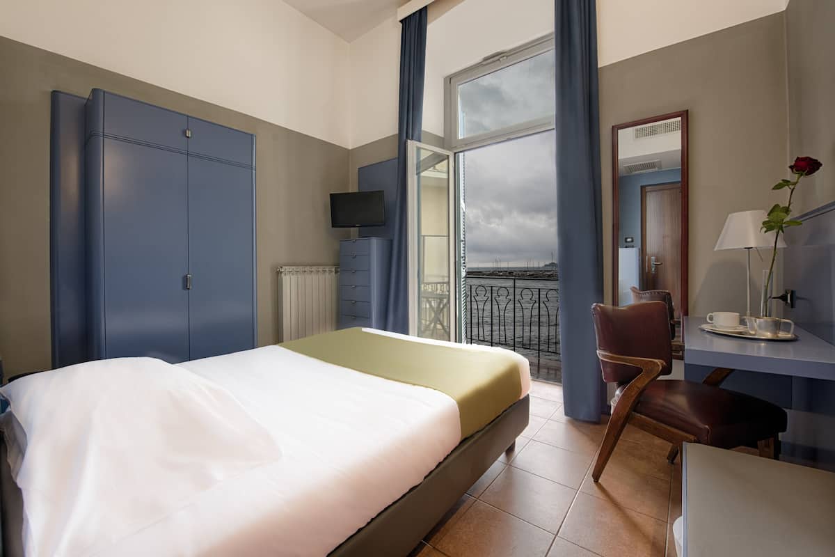 Een hotelkamer met een bed, een bureau met stoel, een televisie en een balkon met uitzicht.