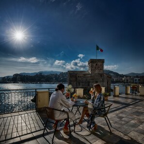 Une terrasse extérieure offrant une vue sur une étendue d’eau, un drapeau et un paysage urbain en arrière-plan.