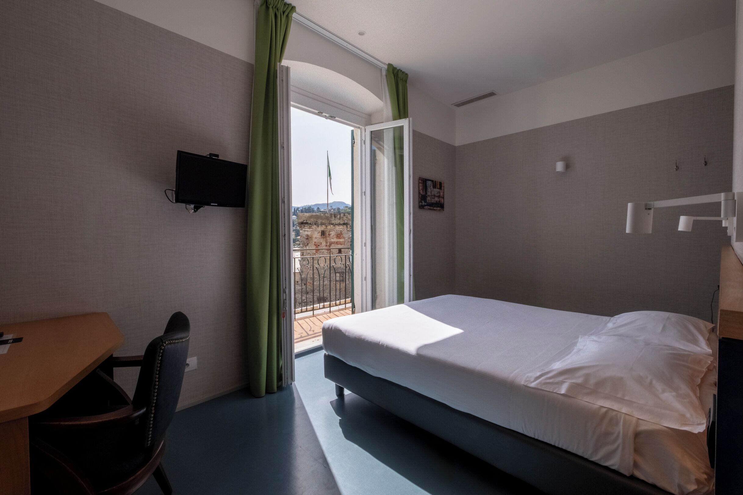Een hotelkamer met een bed, een bureau, een stoel, een televisie en een balkon met uitzicht.