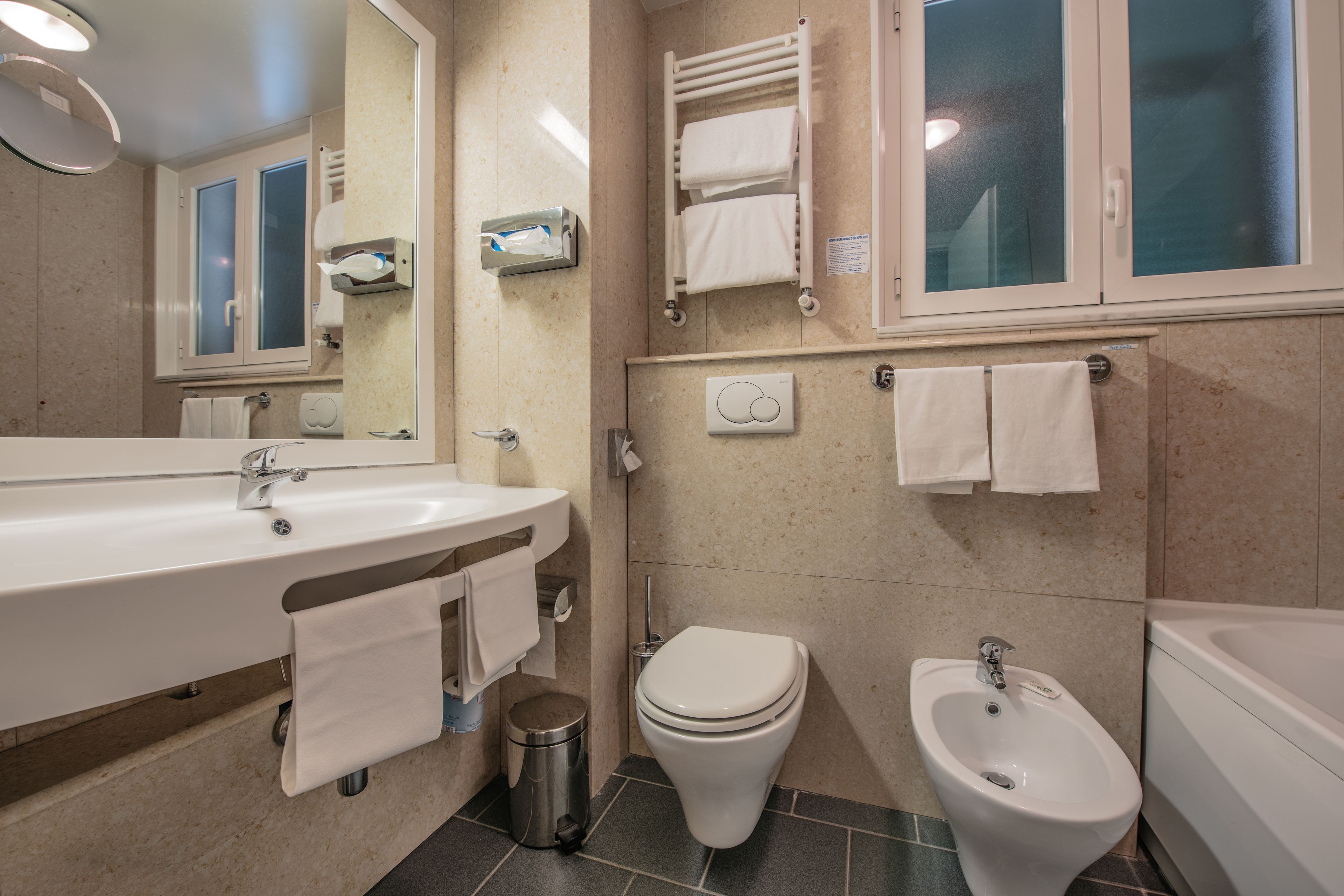 A modern bathroom with a sink, toilet, bidet, and towel racks.