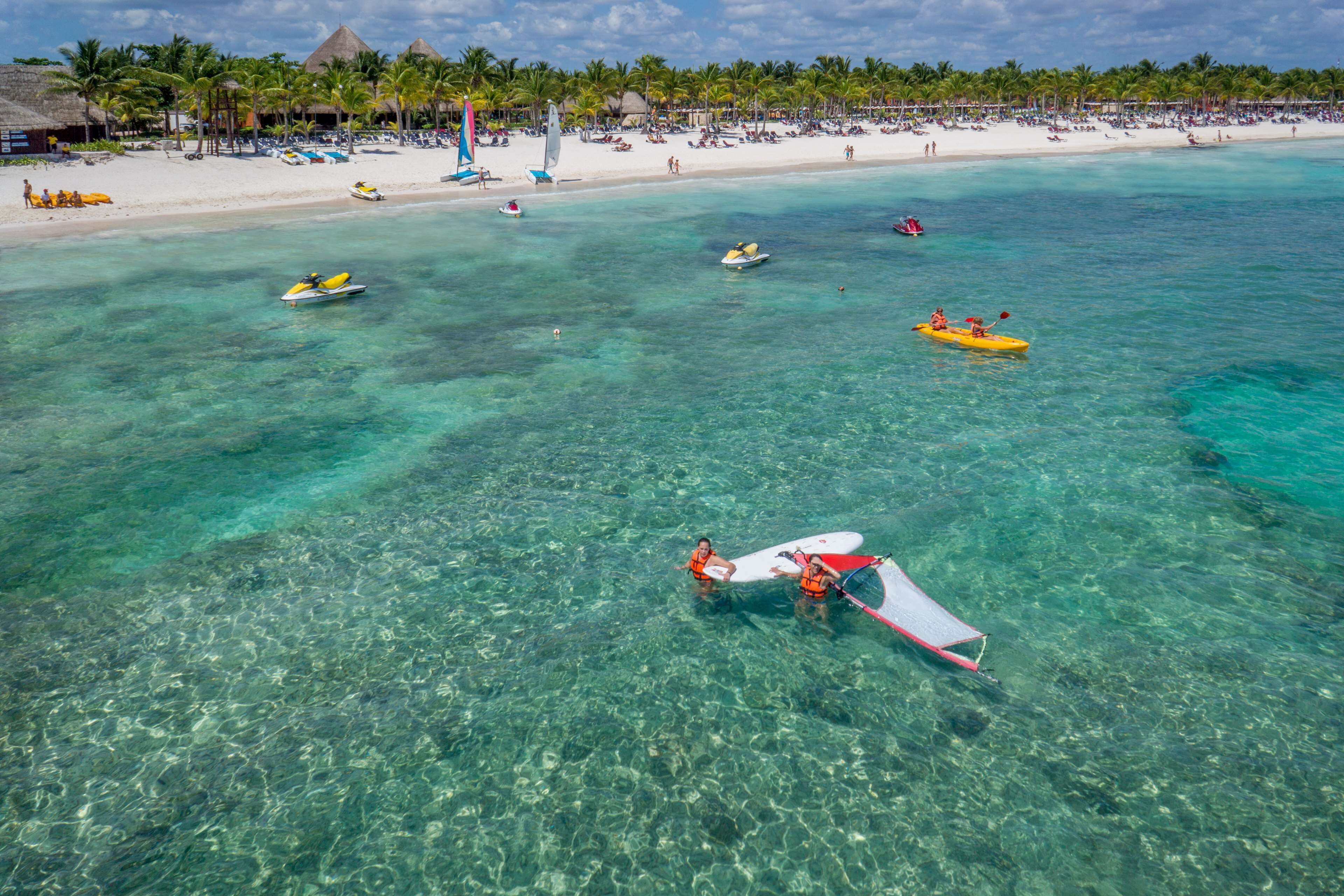 Une plage à l’eau turquoise et limpide, un rivage sablonneux et plusieurs bateaux.