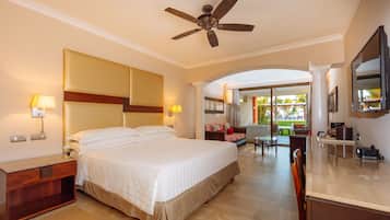 Quarto de hotel com uma cama grande, um ventilador de teto, uma escrivaninha com abajur, uma televisão e vista para a área externa.
