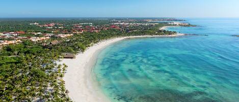 A coastal resort with a sandy beach, clear turquoise waters, and dense greenery.