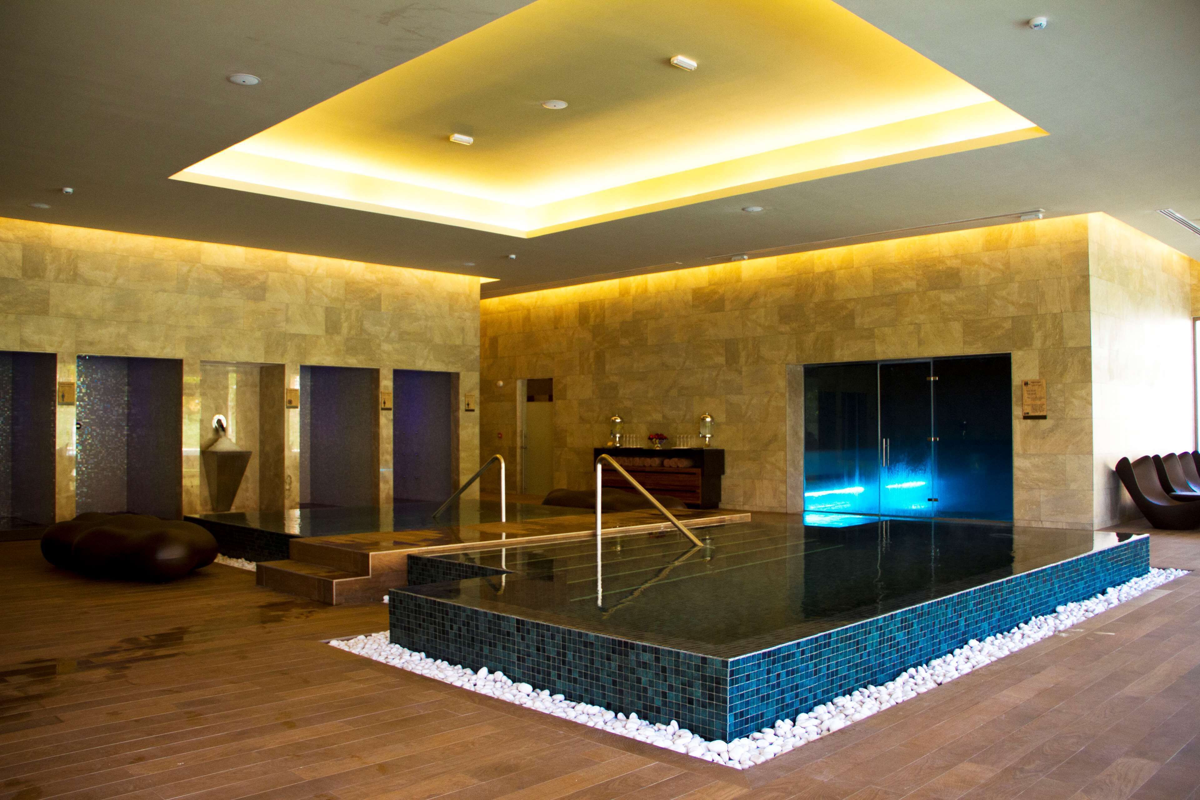 A modern spa with a heated pool, wooden flooring, and stone walls.