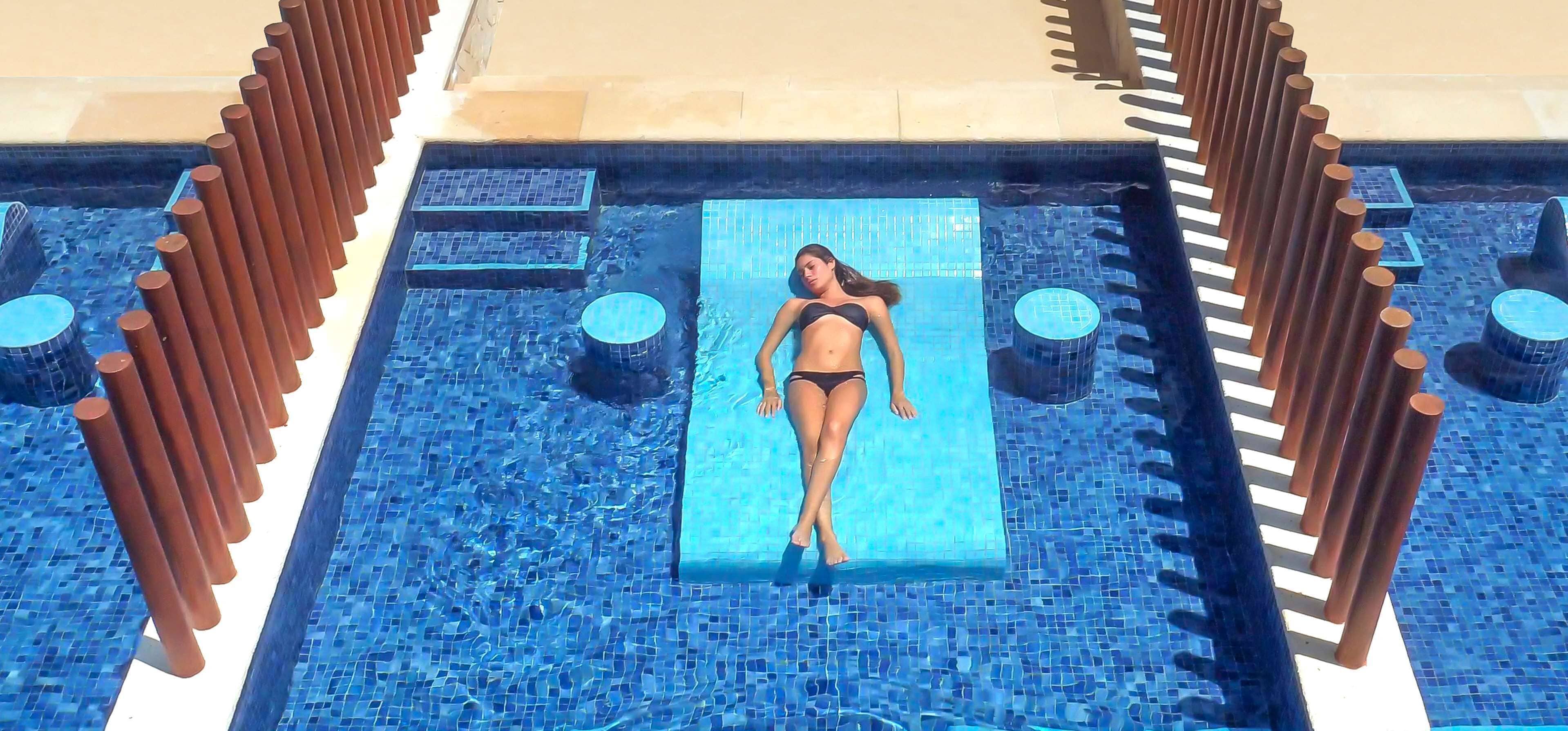Zona de piscina con suelo de baldosas, una plataforma central y estructuras verticales a ambos lados.