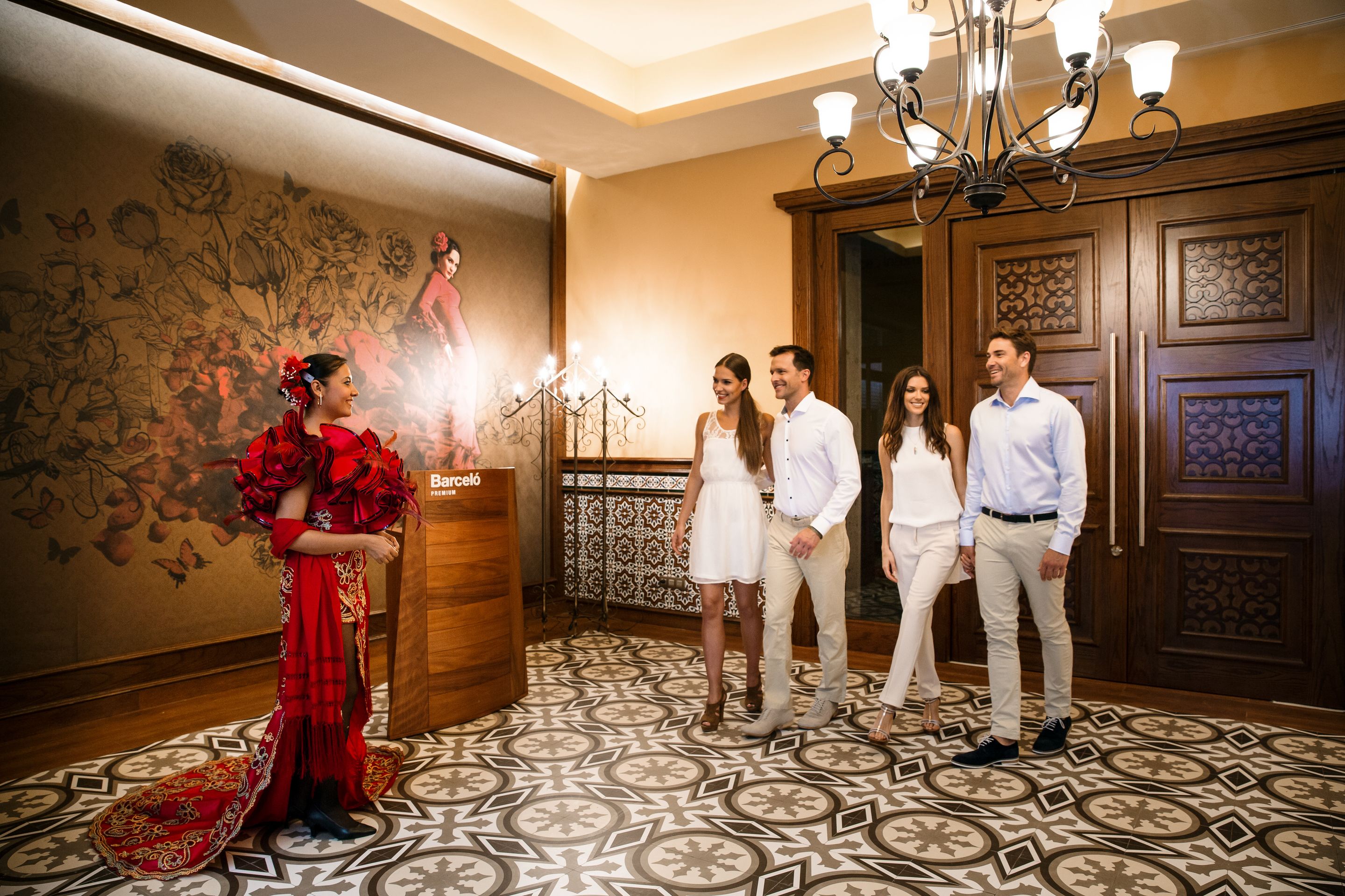 A group of people in a room with patterned flooring, a chandelier, and a wooden door.