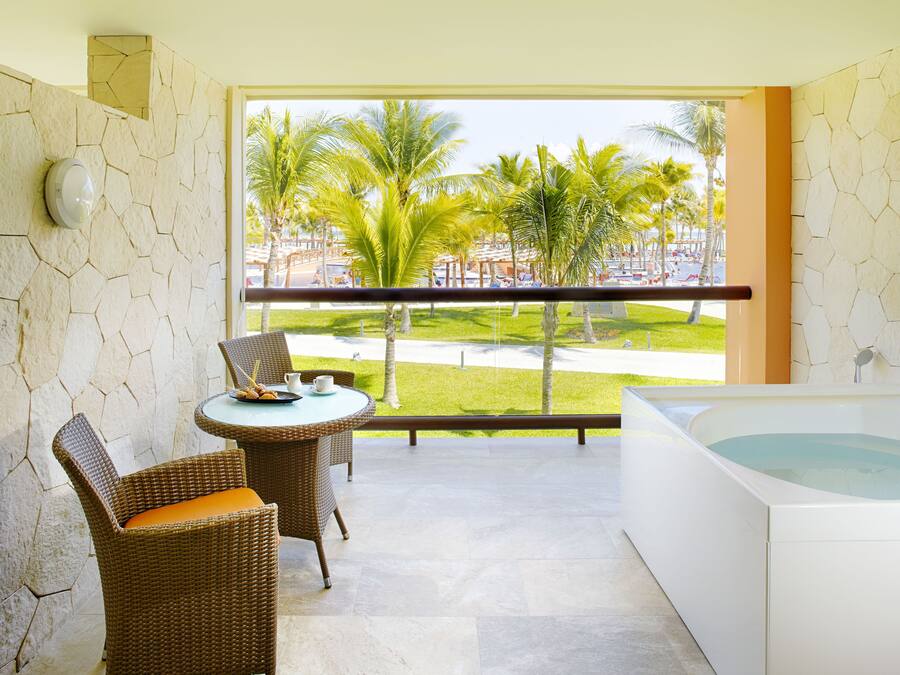Een balkon met rieten meubilair, uitzicht op palmbomen en een jacuzzi.