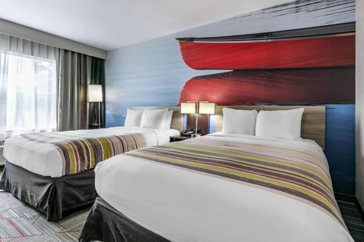 A hotel room with two beds, a large abstract painting on the wall, and a window with curtains.