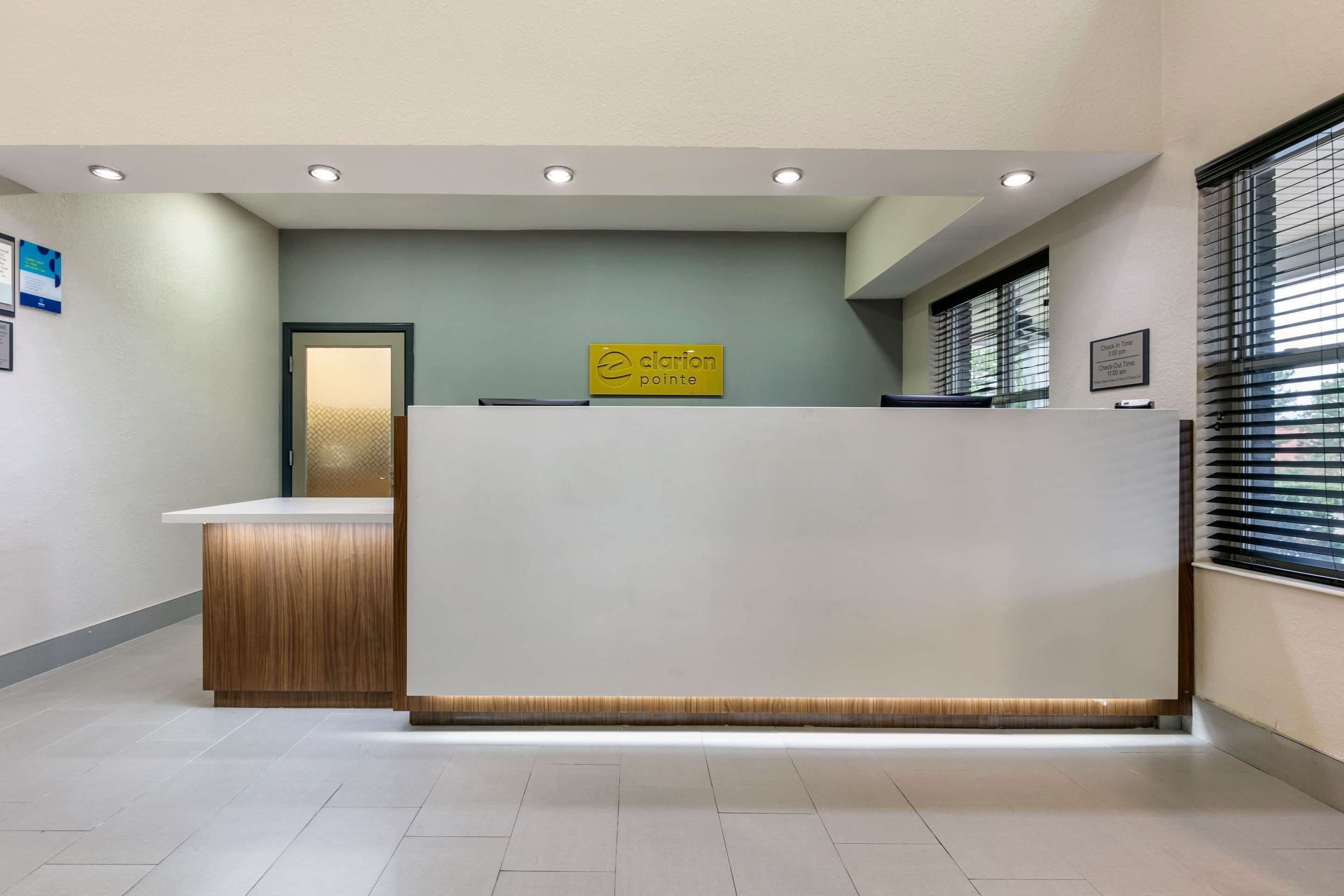 A reception area with a wooden reception desk, a sign reading "Clarion Pointe," and a window with blinds.