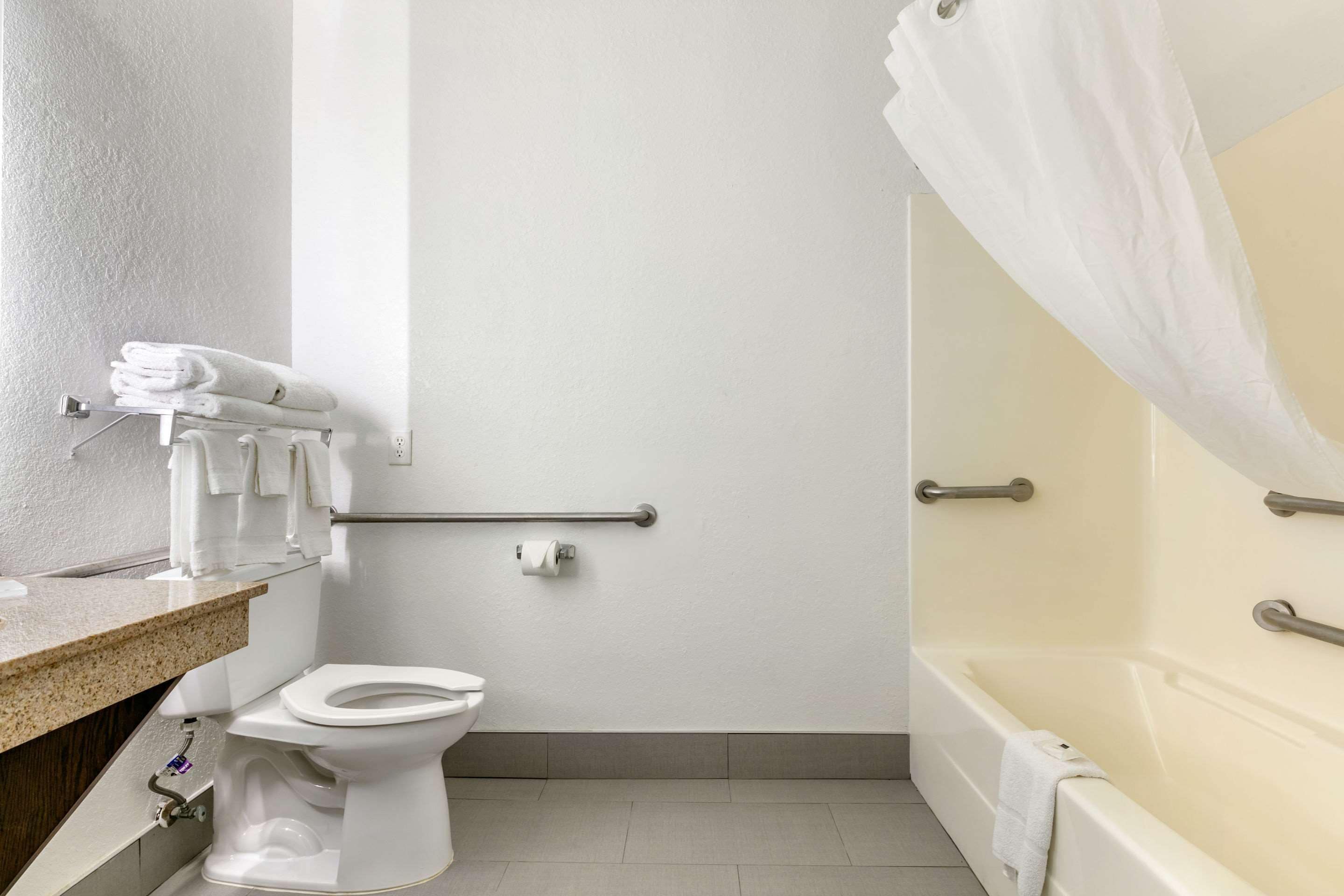 A bathroom with a toilet, a bathtub with a shower curtain, a towel rack, and a handrail.