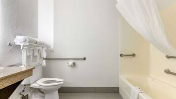 A bathroom with a toilet, a bathtub with a shower curtain, a towel rack, and a handrail.
