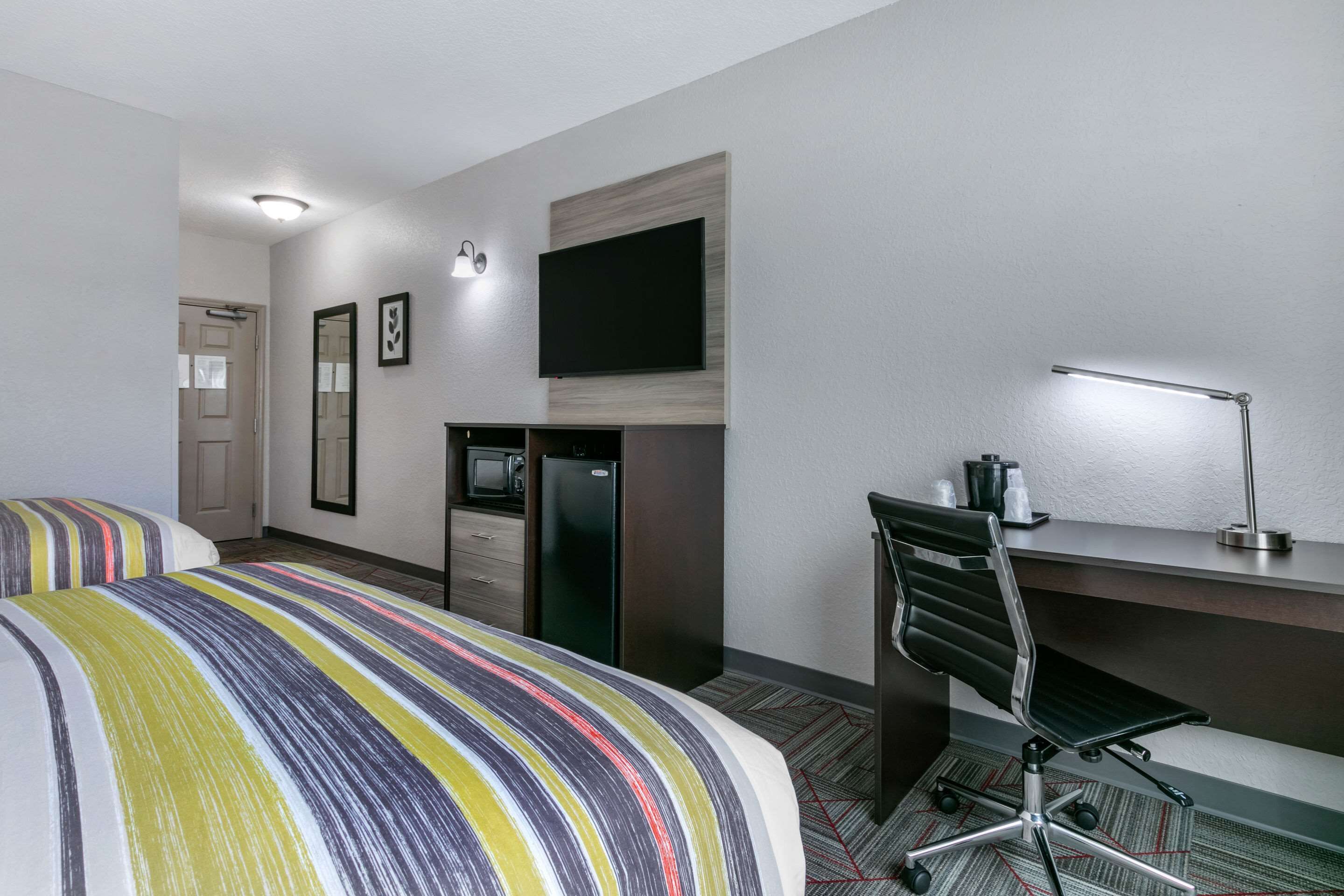 Ein Hotelzimmer mit Bett, Schreibtisch, Stuhl, Fernseher, Mikrowelle und Kühlschrank.