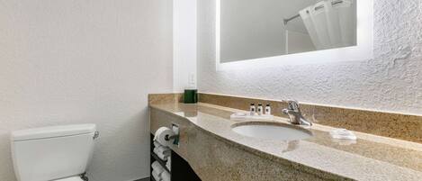 Un baño con inodoro blanco, lavabo con encimera de granito y un espejo grande.