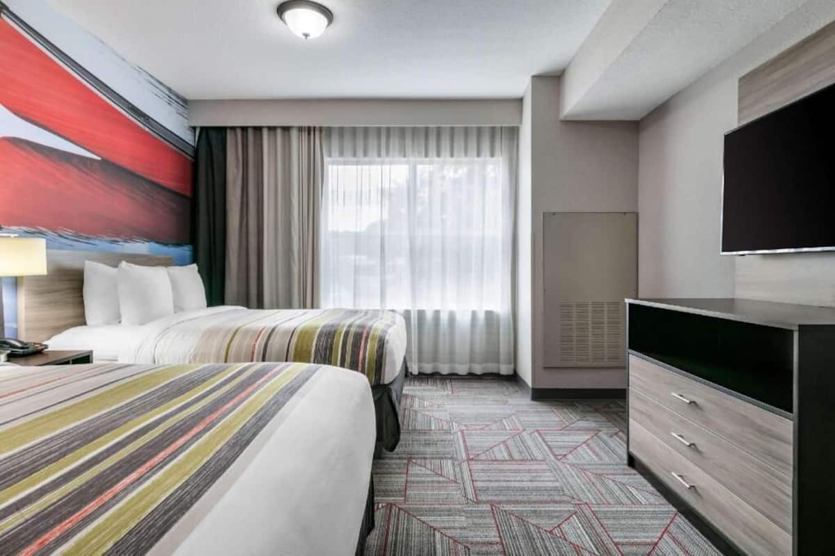 A hotel room with two beds, a large window with curtains, a flat-screen TV, and a desk with drawers.