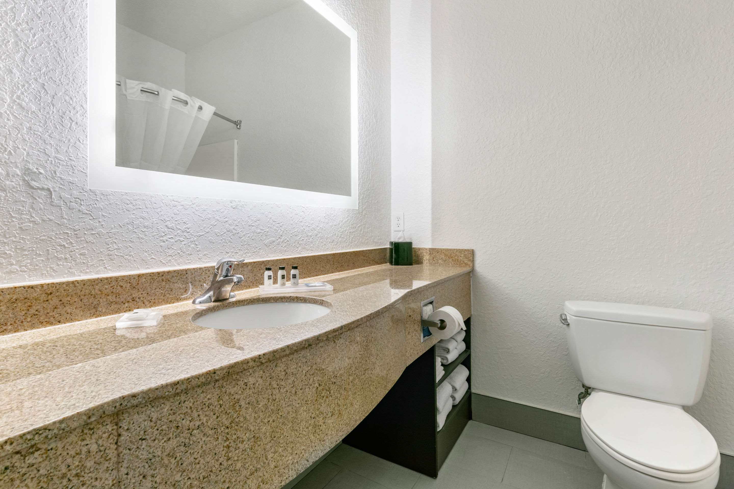 Un baño con lavamanos de encimera de granito, un espejo y un inodoro.