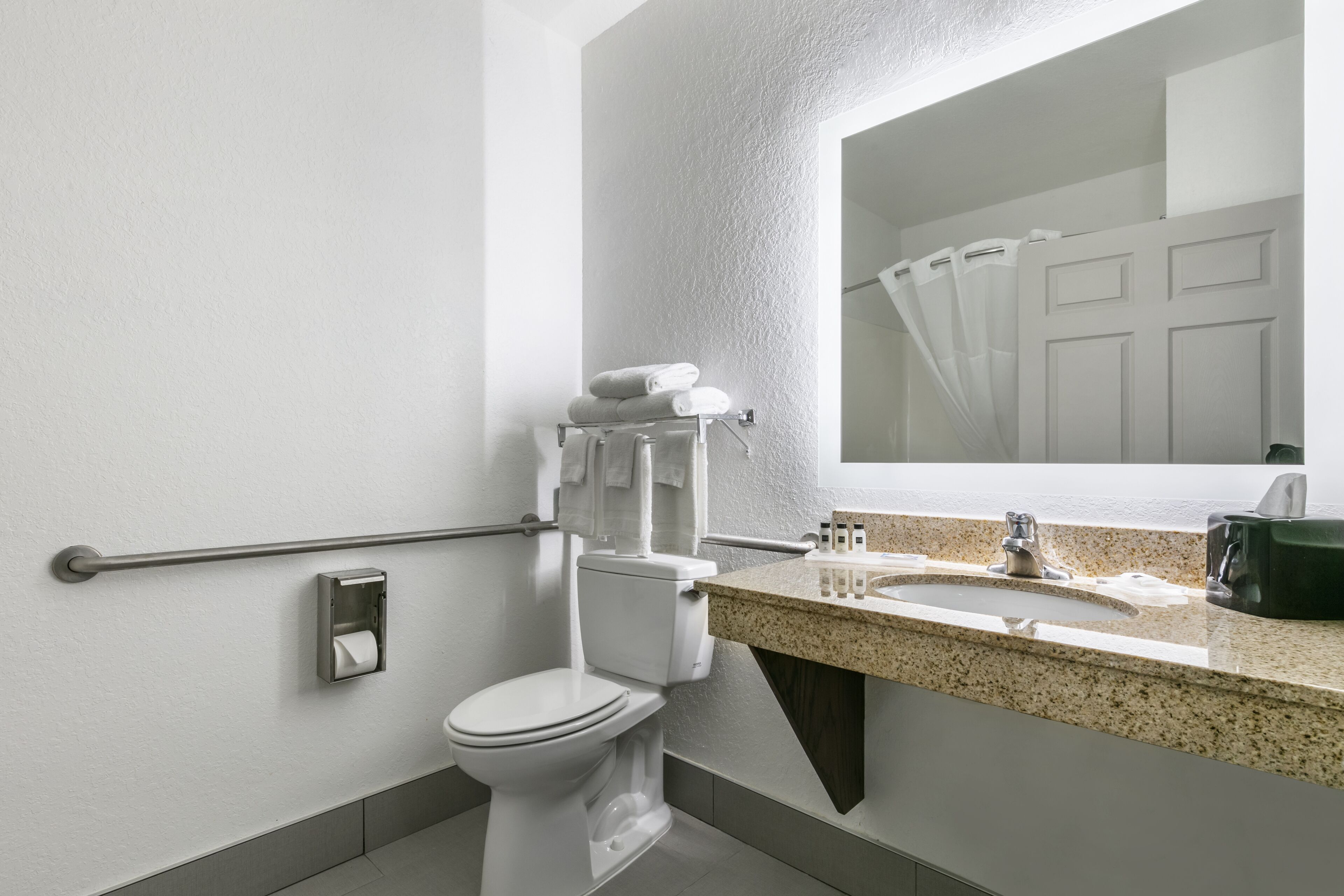 A modern bathroom with a toilet, hand dryer, towel rack, sink, and a mirror.