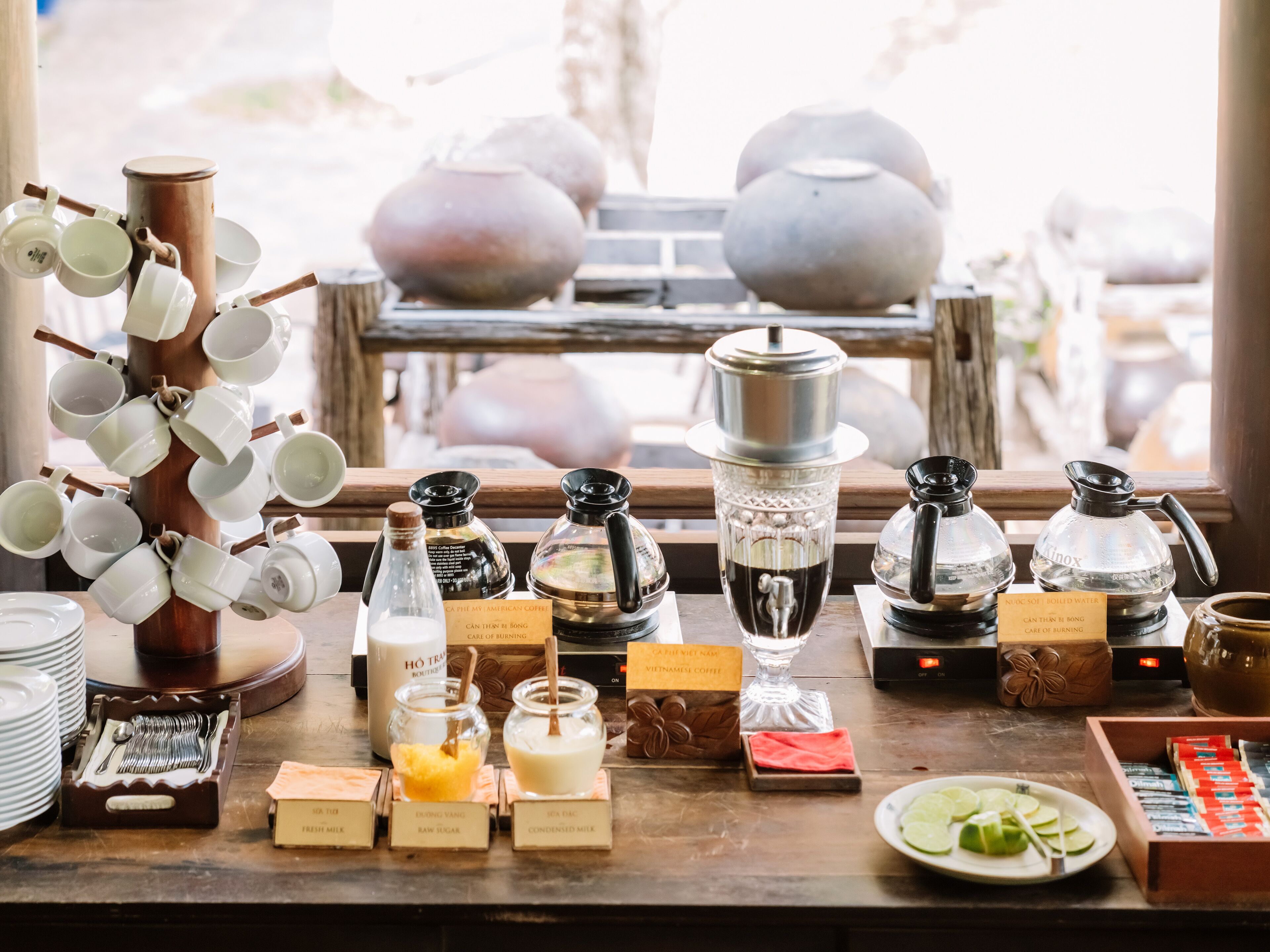 A coffee station with various brewing equipment and labeled containers of milk and sugar.