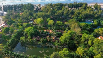 Vista aérea de un resort tropical con abundante vegetación, una piscina y una playa.