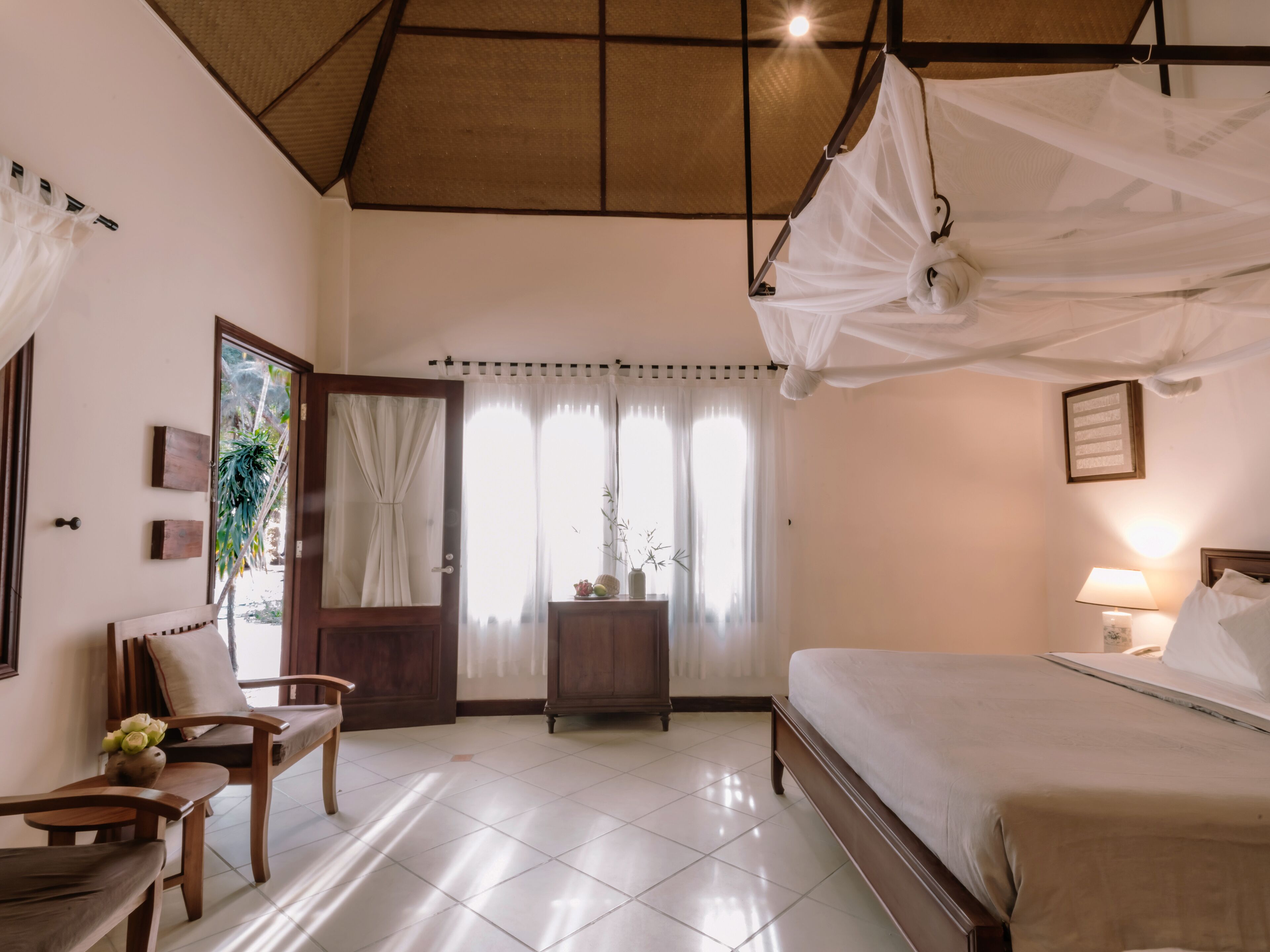 A bedroom with a bed, a chair, a bedside table, a lamp, and a window with curtains.