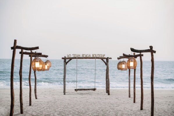 Een houten schommel met een bord waarop staat: "HO TRAM BEACH BOUTIQUE" aan het strand.