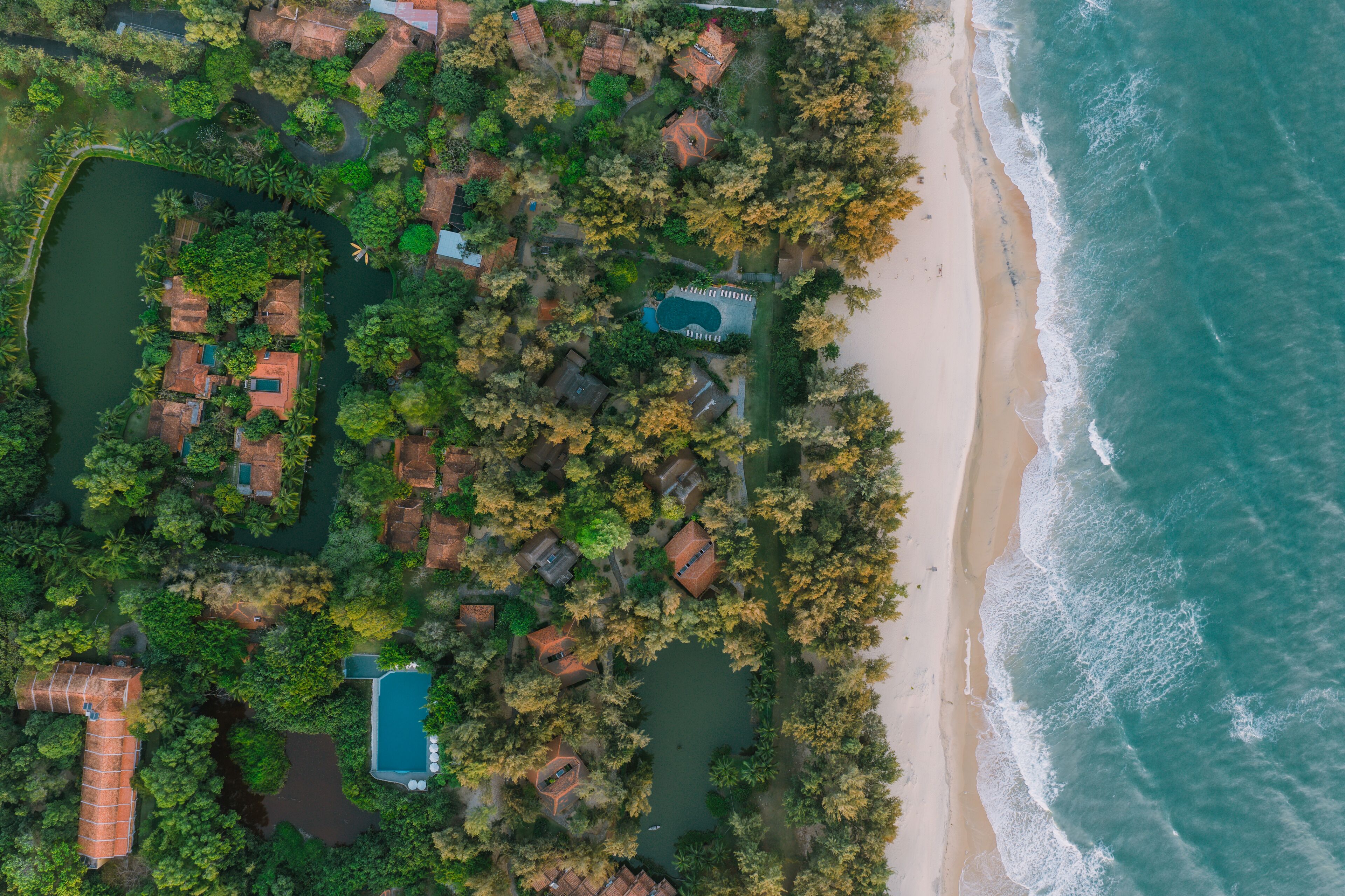 An aerial view of a coastal property with multiple buildings, a swimming pool, and a beach.