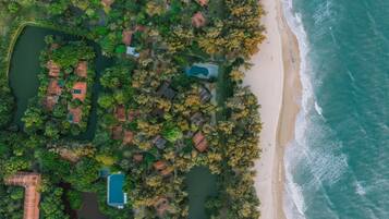 An aerial view of a coastal property with multiple buildings, a swimming pool, and a beach.