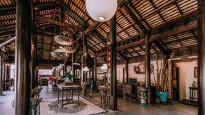 Un hall d’entrée spacieux, doté de hauts plafonds, de poutres en bois et d’une décoration traditionnelle comprenant des lanternes suspendues et une grande plante en pot.
