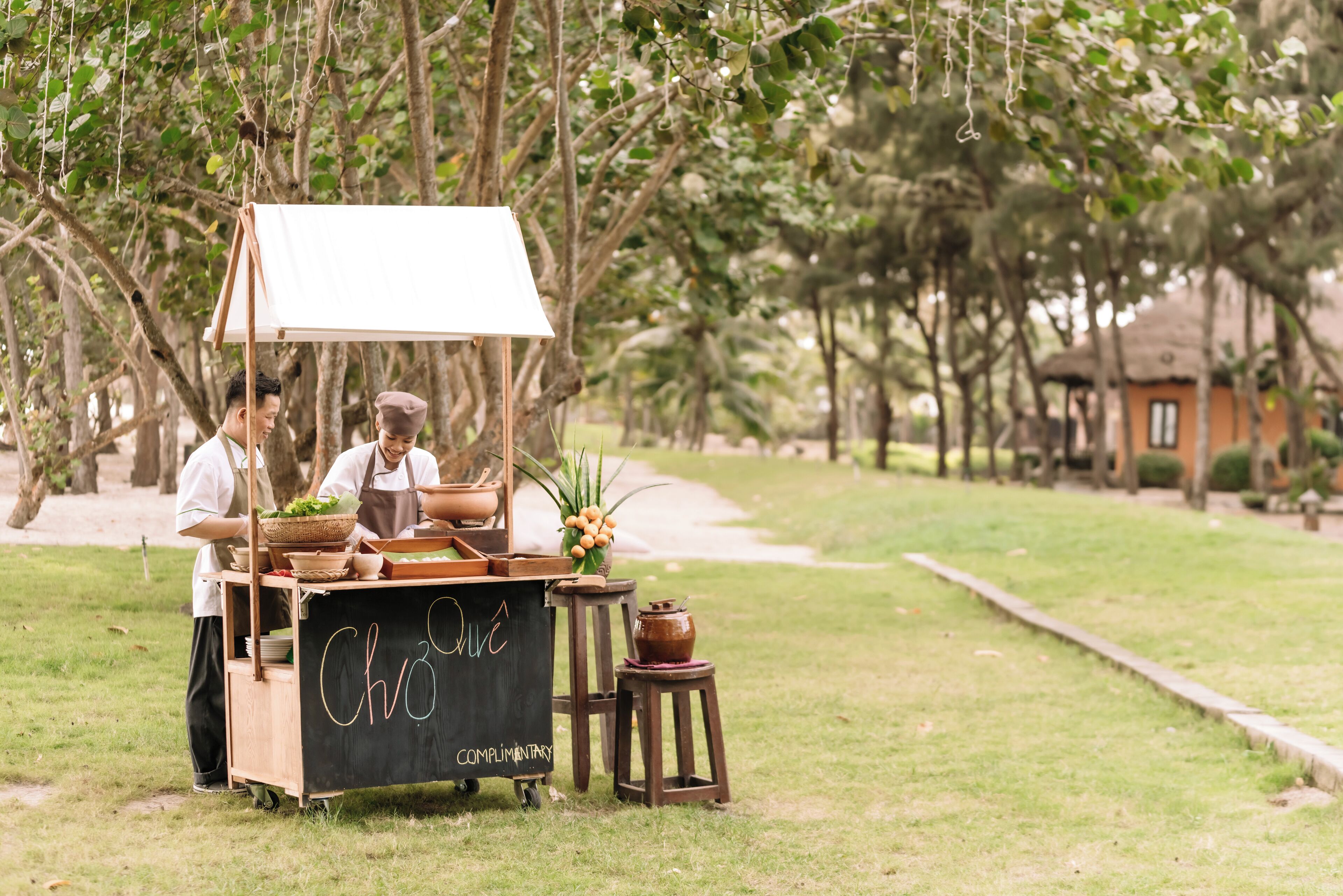A food cart with a chalkboard sign, surrounded by trees and a pathway.