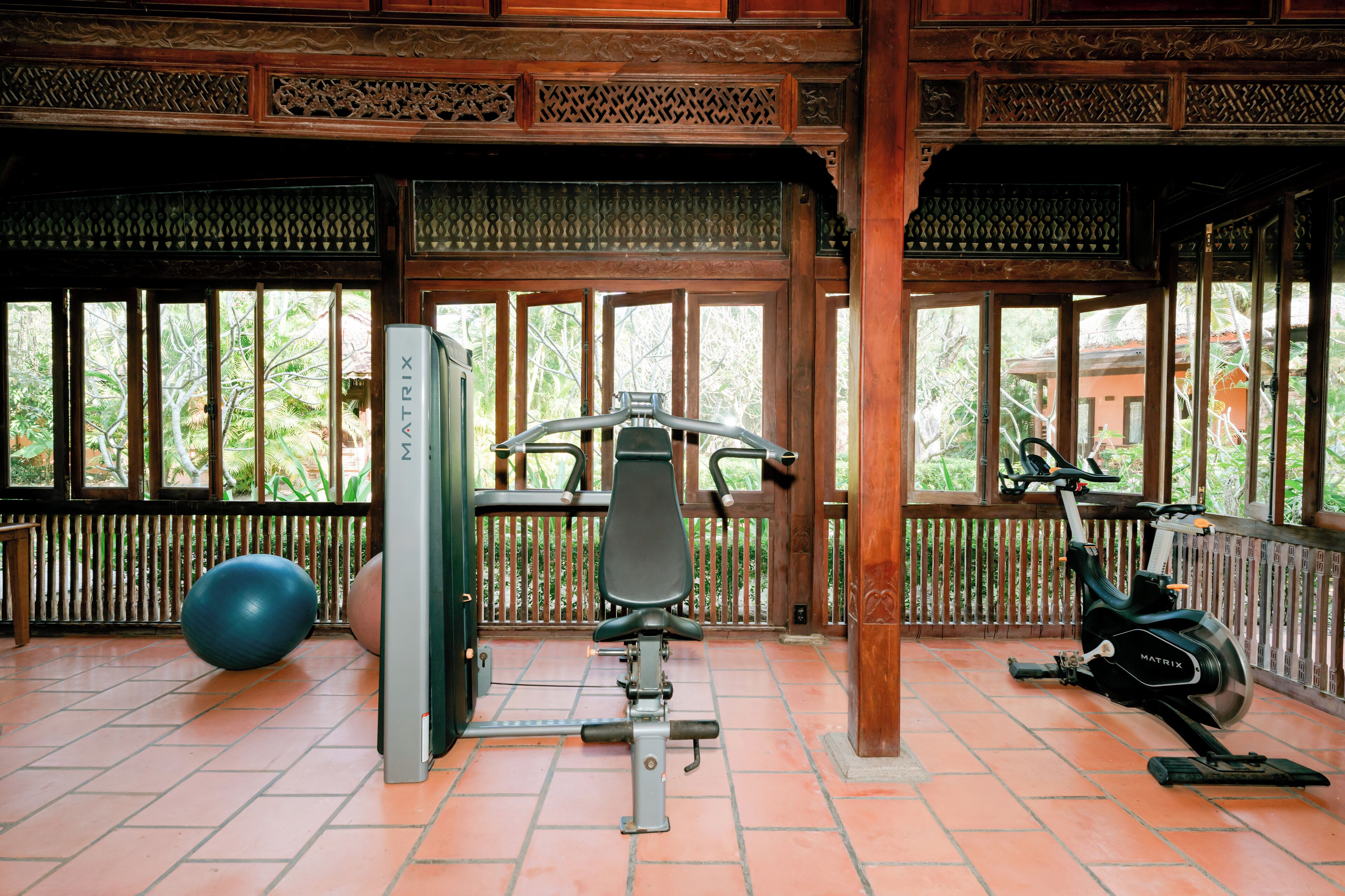 Un gimnasio con equipo de ejercicio, una pelota grande y vistas a zonas verdes a través de amplios ventanales.