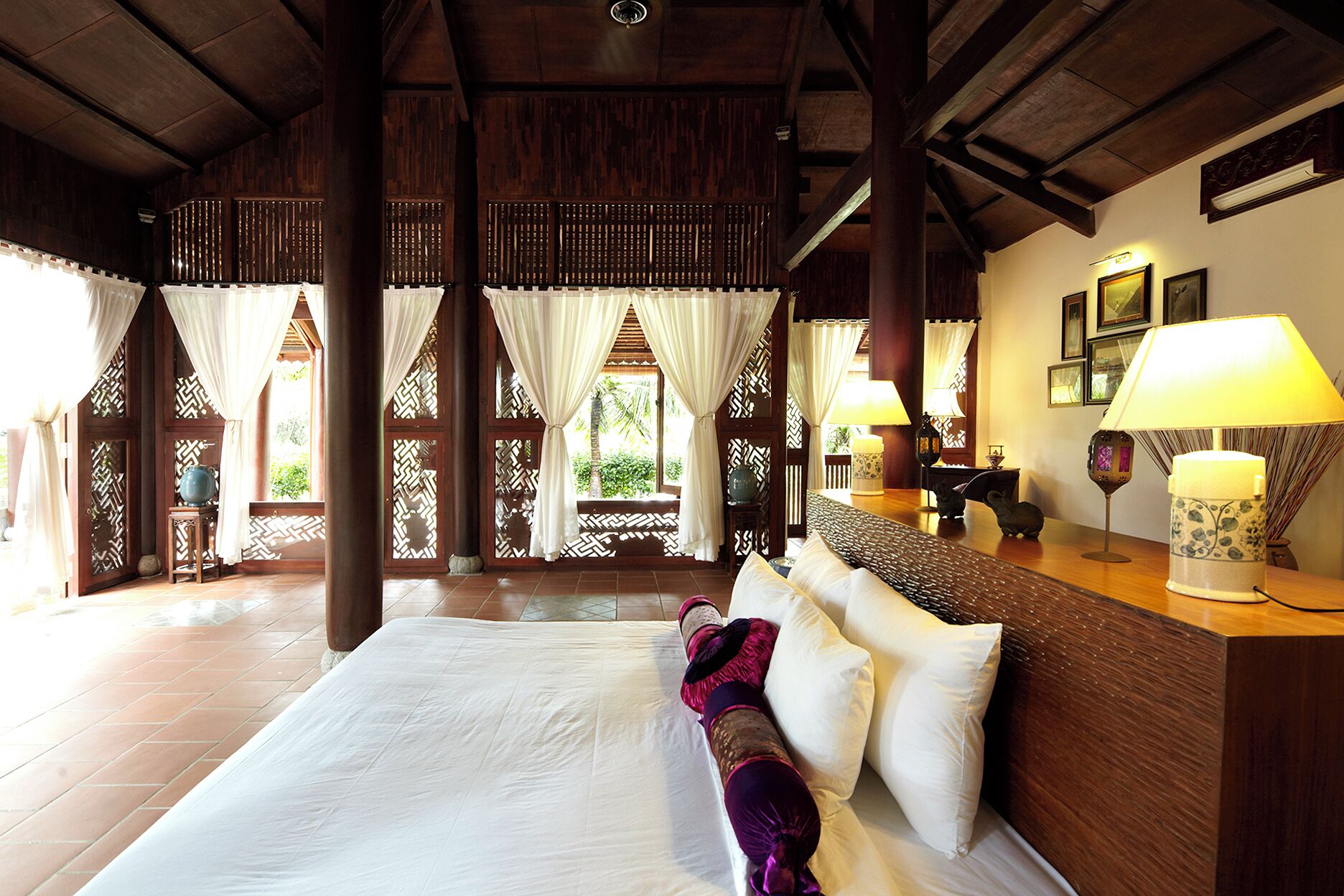 A spacious room with a large bed, wooden beams, and a view of greenery outside.
