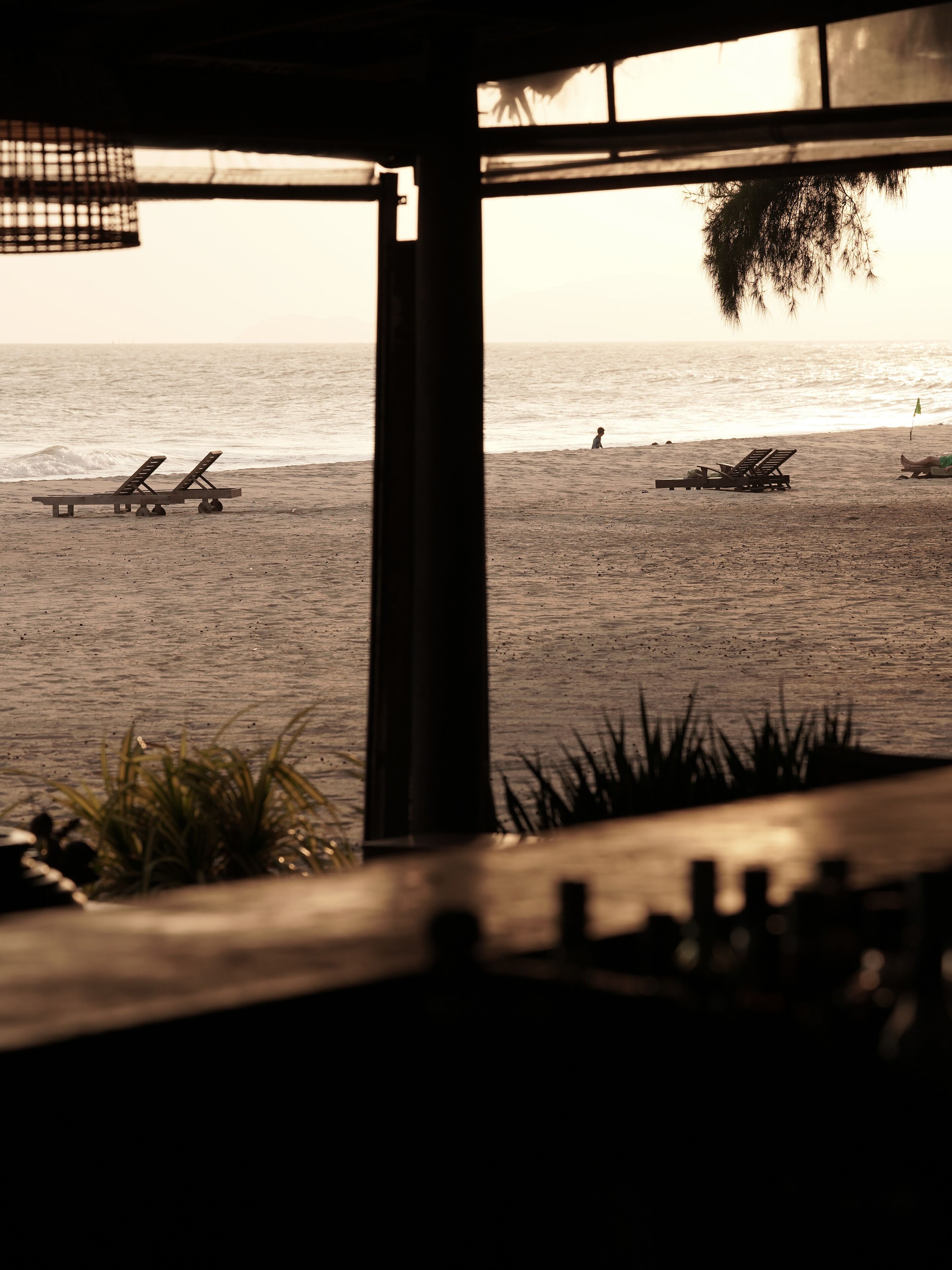 A beach view from a covered area with lounge chairs and a view of the ocean.