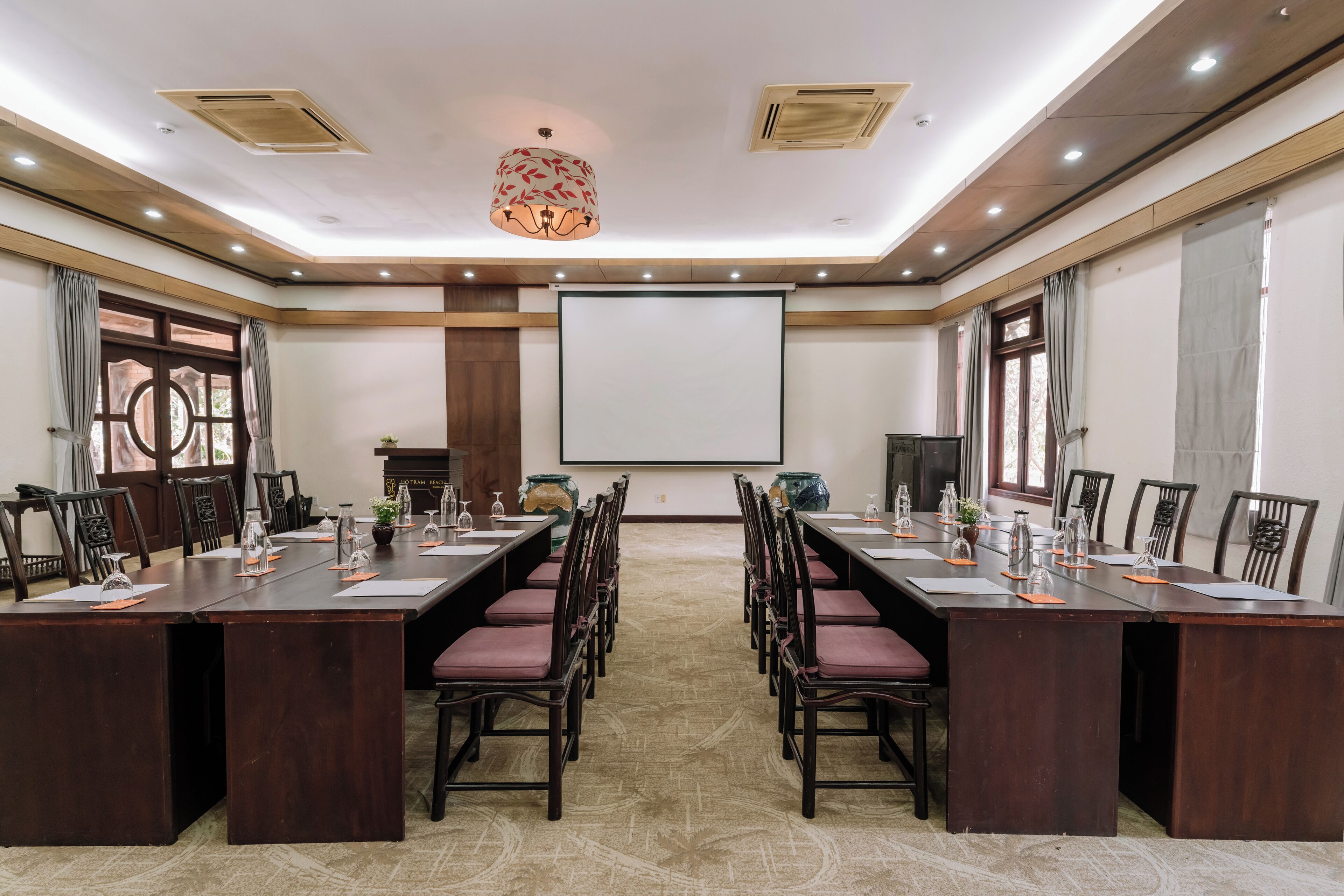A conference room with a long table, chairs, a projector screen, and a decorative chandelier.