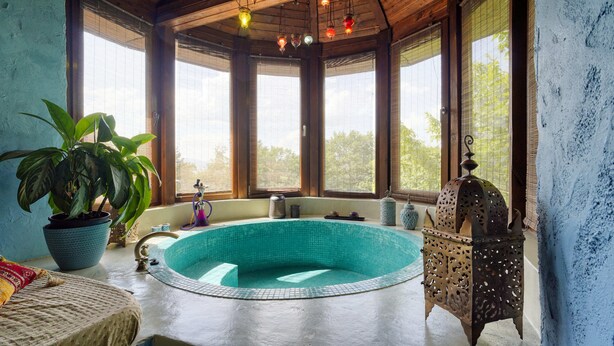 Une piscine circulaire, dont l’intérieur est revêtu de carreaux, entourée de poutres en bois et dotée de grandes fenêtres.