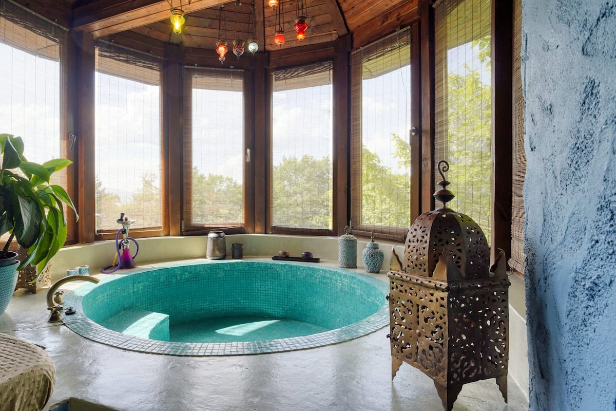 Una piscina circular con revestimiento de baldosas, rodeada de vigas de madera y amplias ventanas.