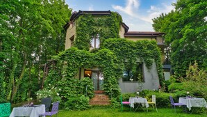 Un bâtiment aux murs recouverts de lierre et un jardin aménagé avec des tables et des chaises pour prendre les repas.