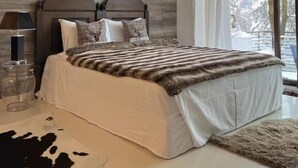 Une chambre moderne avec un grand lit, une tête de lit en bois et une vue sur un paysage enneigé par la fenêtre.