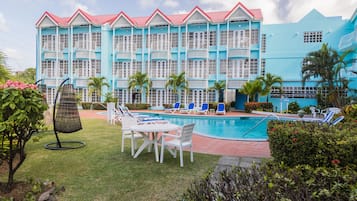 Un hotel con zona de piscina, mobiliario exterior y un edificio grande con balcones.