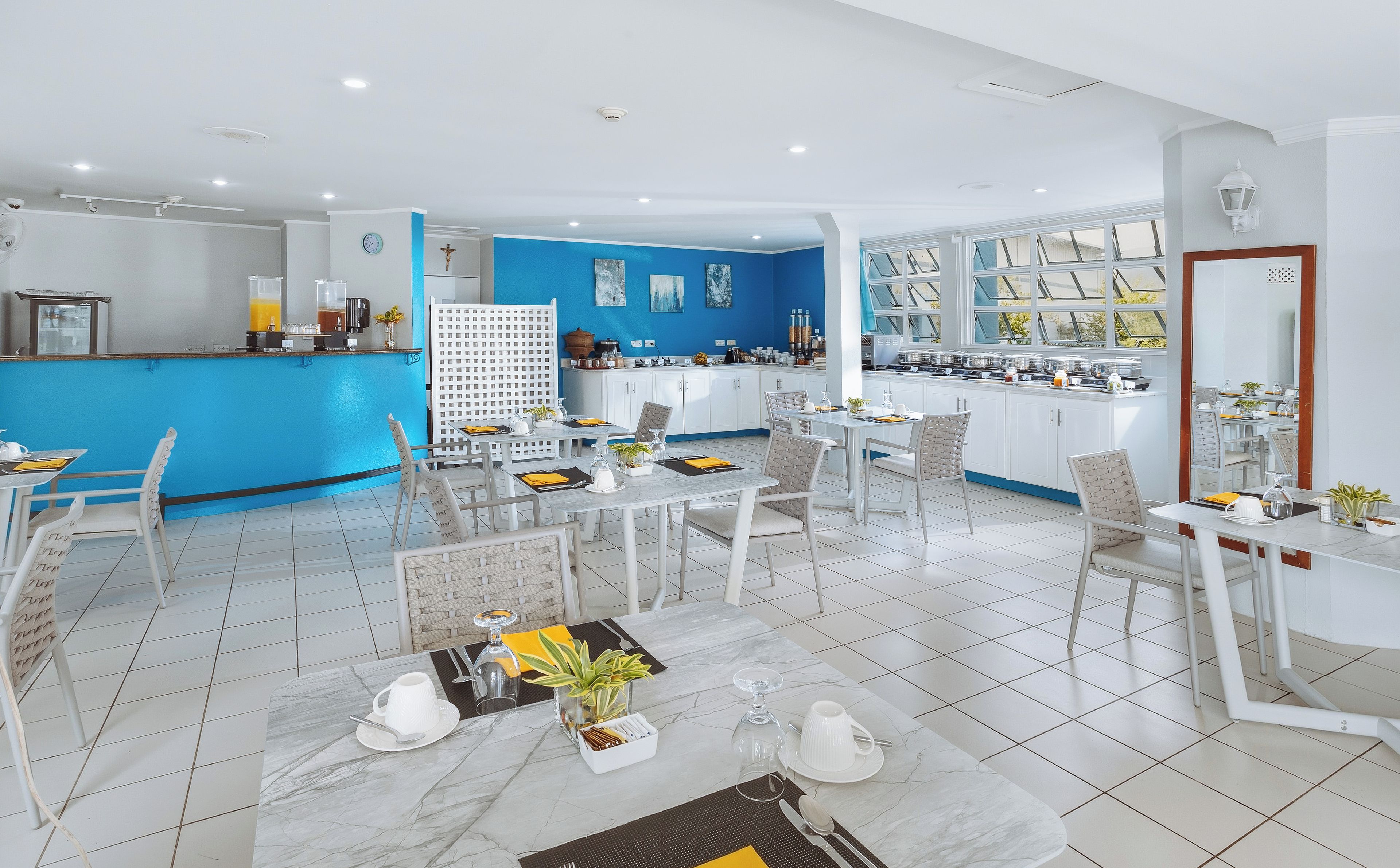 A modern kitchen with white cabinets, a blue accent wall, and a dining area with white chairs and a marble table.