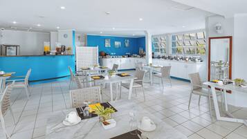 Een moderne keuken met witte kasten, een blauwe accentmuur, en een eethoek met witte stoelen en een marmeren tafel.