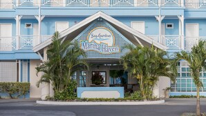 Un hôtel à la façade bleue, une enseigne indiquant « Bay-Gardens Marina Haven », et une balustrade blanche.