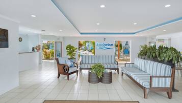 A hotel lobby with a reception desk, seating area, and a sign for 'Bay Gardens'.