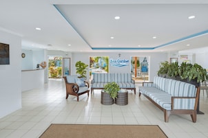 Een hotel lobby met een receptiebalie, een zithoek en een bordje met 'Bay Gardens'.