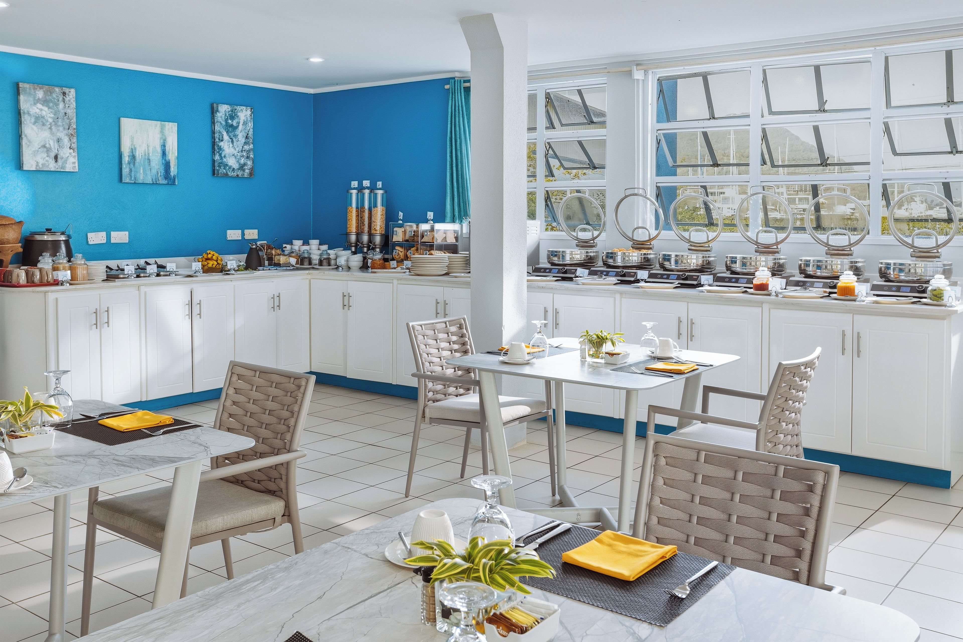 Un espace de salle à manger lumineux, avec des meubles blancs, un mur d’accent bleu et une vue d égagée grâce à de grandes fenêtres.