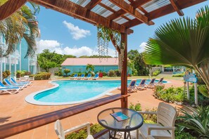 Un espace piscine avec des chaises longues, un coin salon abrité et un bâtiment en arrière-plan.