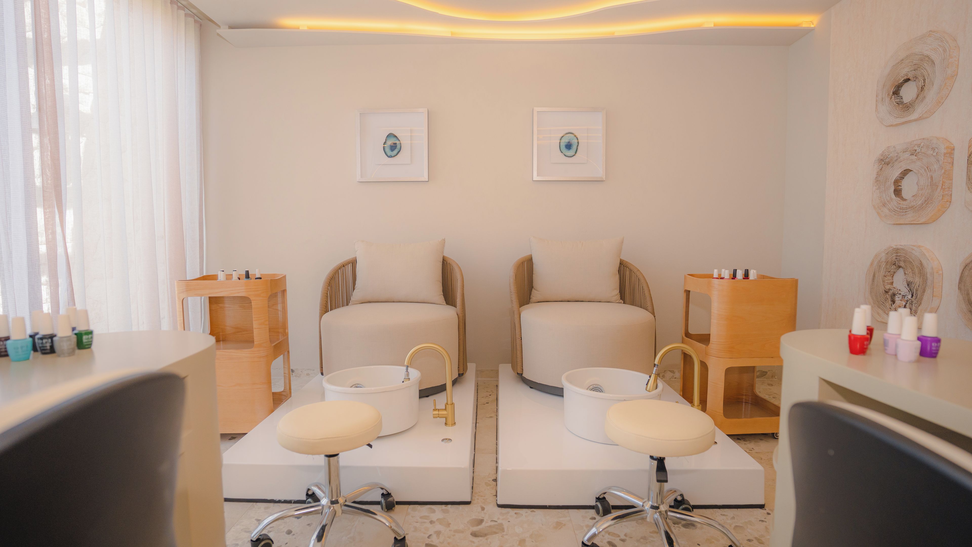 A room with two chairs, a small table, and a wall-mounted shelf with nail polish.