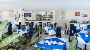 Un restaurant avec des tables dressées pour le service, un coin bar et un présentoir où sont exposées différentes bouteilles.